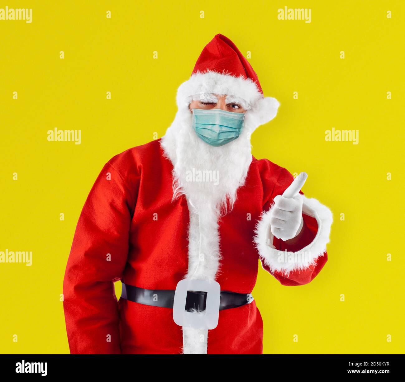 Le Père Noël le Père Noël avec masque chirurgical montre le pouce vers le haut montre le pouce vers le haut sur fond jaune. Banque D'Images