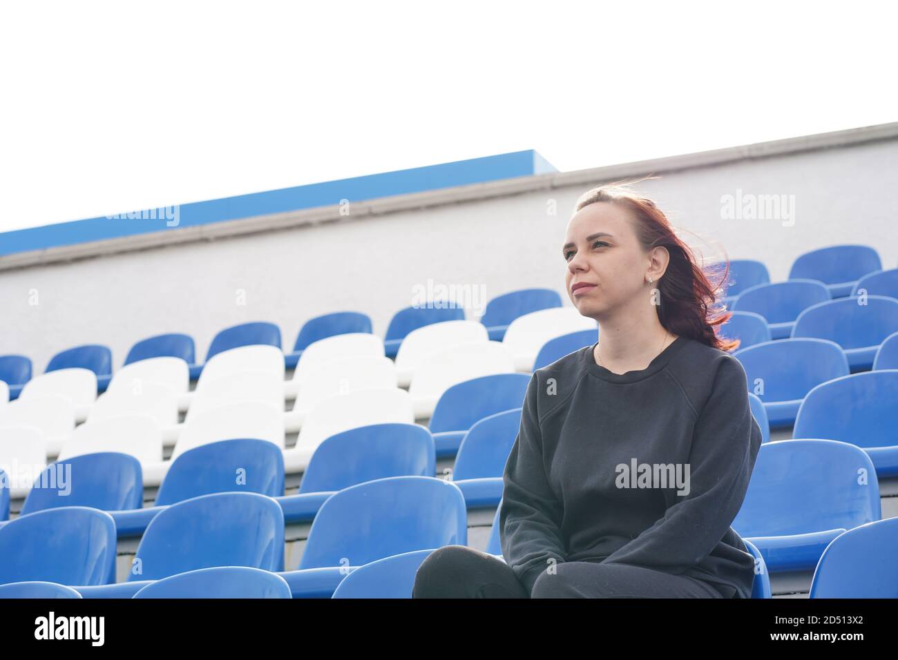 Une jeune femme dans un survêtement noir avec de longs cheveux se trouve sur le stade seul et regarde un sport jeu Banque D'Images