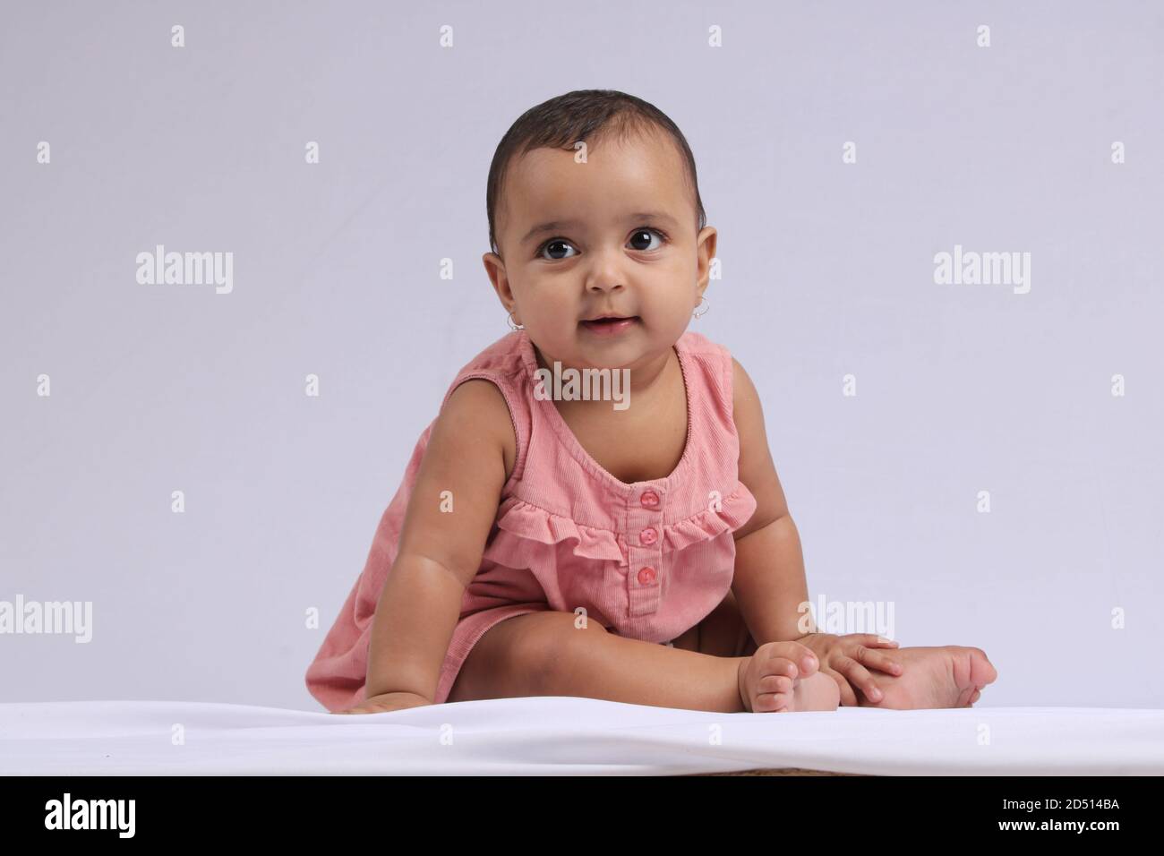 Mignon Indien gai bébé assis et souriant sur blanc. Banque D'Images