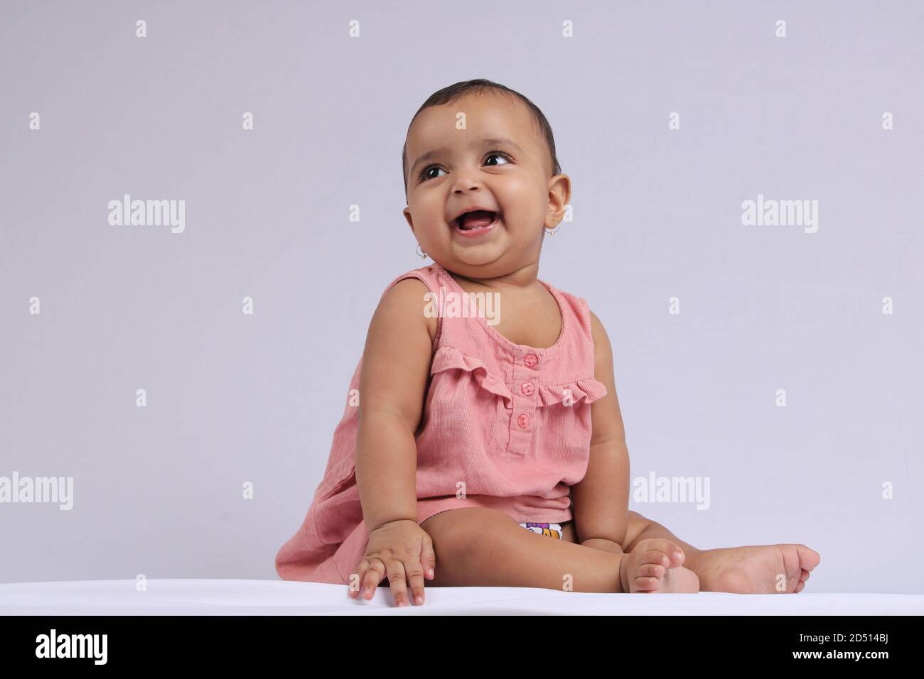 Mignon Indien gai bébé assis et souriant sur blanc. Banque D'Images