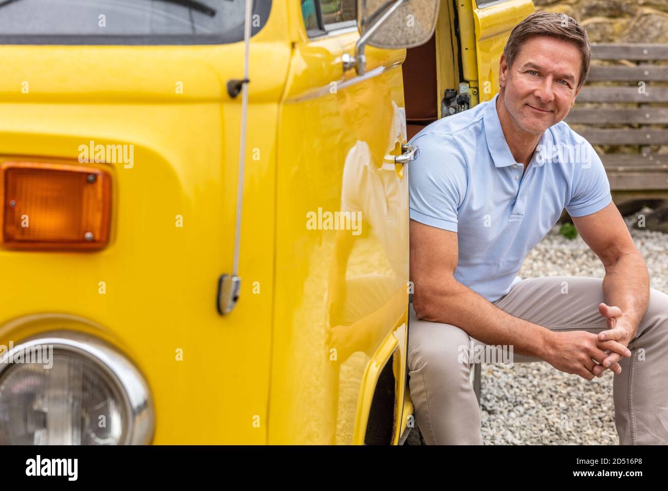 Portrait d'un homme d'âge moyen attrayant, réussi et souriant, portant un polo bleu, assis dans la porte d'une camionnette ou d'un camion Banque D'Images