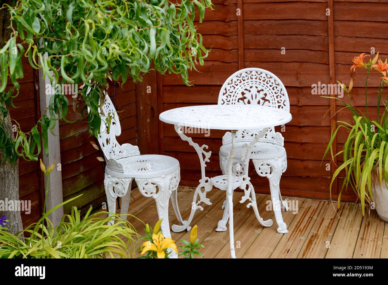 Jolie table de bistro blanche et chaises disposées à l'extérieur sur du  bois terrasse entourée d'un patio en pots et de saules à l'orange et lys  tigres jaunes Photo Stock - Alamy