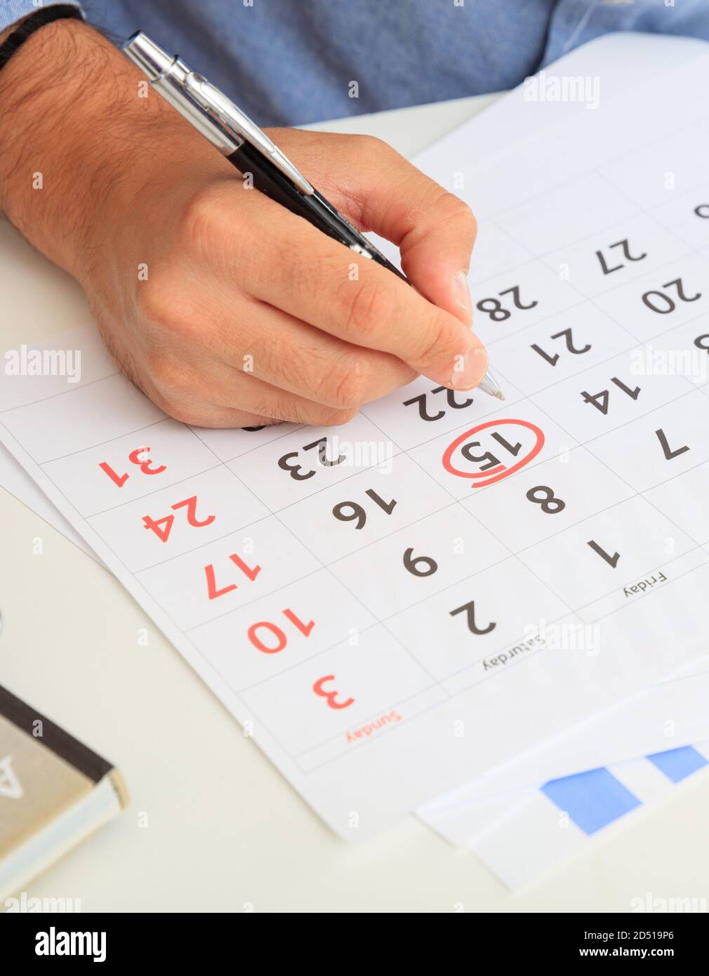 Homme main marqué 15ème jour sur le calendrier, arrière-plan de bureau. Quinzième date entourée d'un stylo rouge dans le planificateur. Gros plan, vue verticale. Banque D'Images