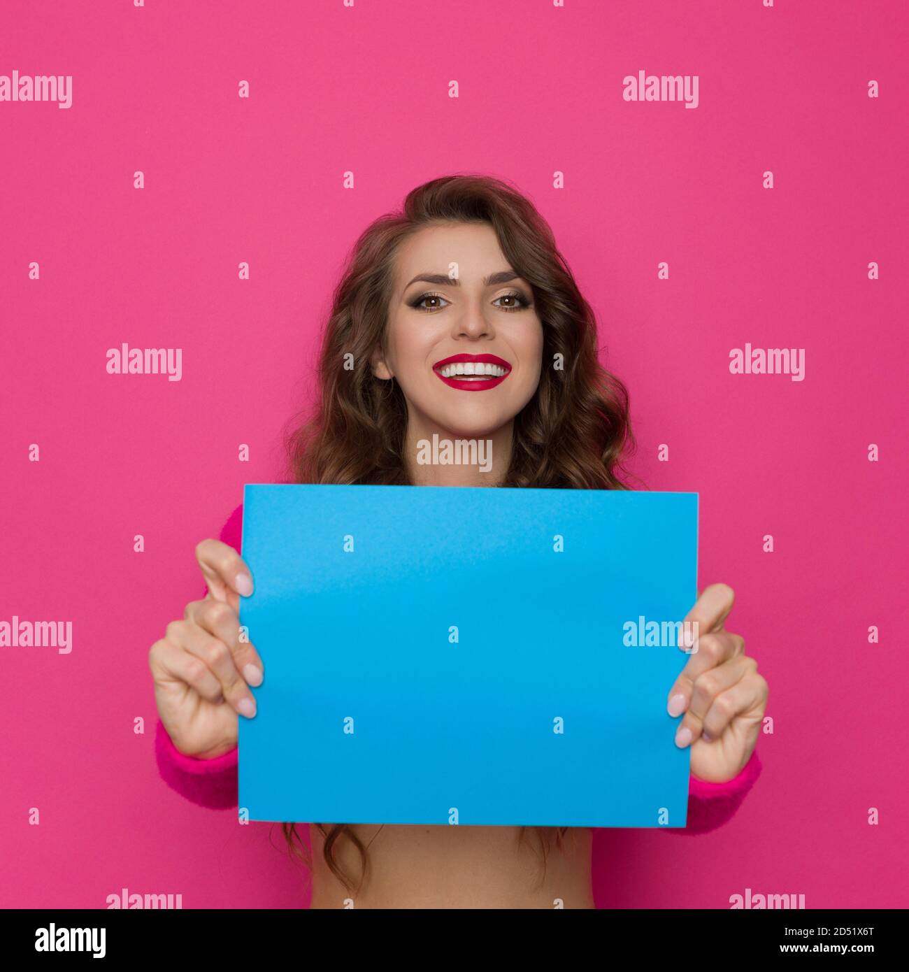 Une jeune femme souriante tient une feuille de papier bleue devant elle. Taille haute studio tourné sur fond rose. Banque D'Images
