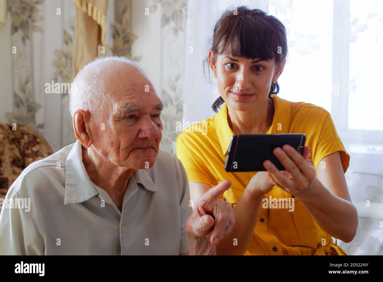 Un homme mature d'apparence européenne avec une jeune femme assise sur le canapé et regardant le téléphone. Payez vos achats par téléphone. Générations. Le Banque D'Images