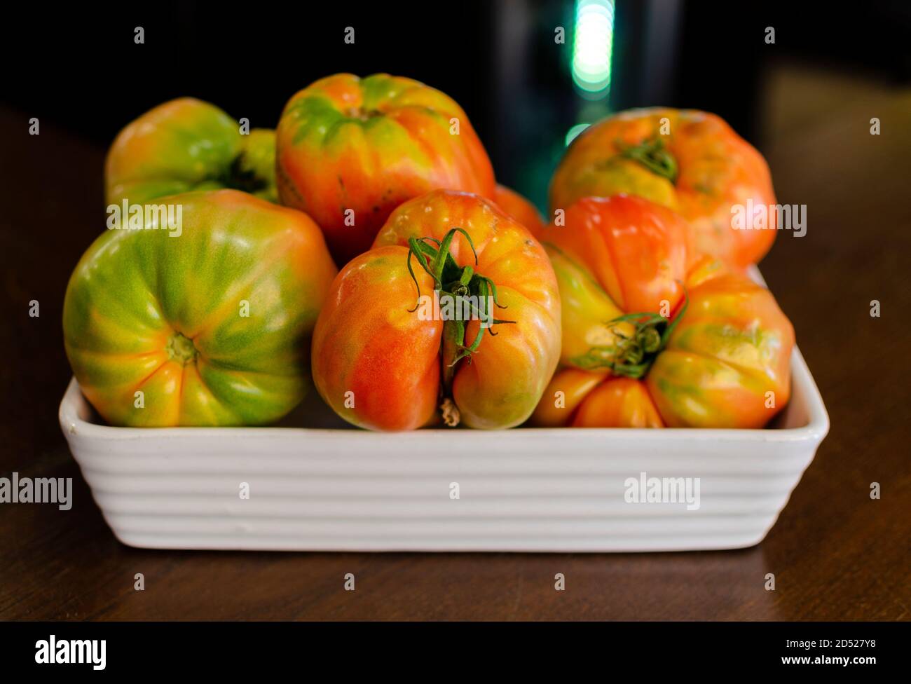 Tomates (Solanum lycopersicum, Lycopersicon esculentum) également connues sous le nom de tomates coeur de boeuf ou de vache dans un récipient blanc sur une table en bois. Sélectif FO Banque D'Images