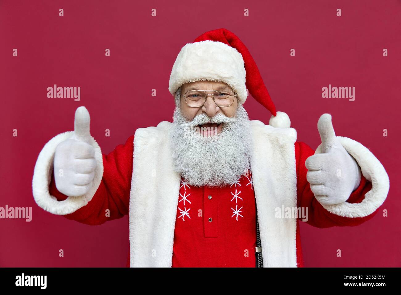 Joyeux Père Noël montrant les pouces isolés sur fond rouge. Banque D'Images