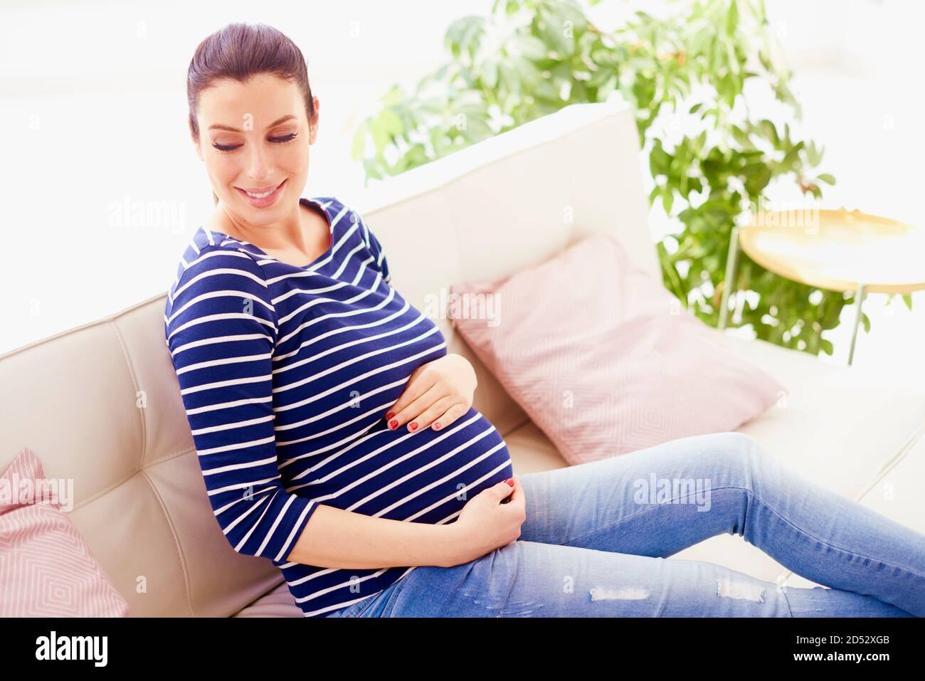 Prise de vue en grand angle d'une belle femme enceinte avec les mains sur la  sonnette de son bébé qui aime sa grossesse tout en se relaxant sur le canapé  à la