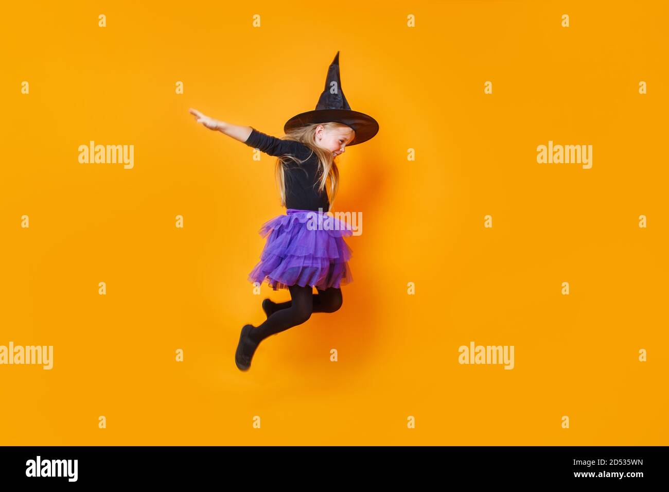 Une fille heureuse en costume de sorcière sautant sur fond orange Banque D'Images