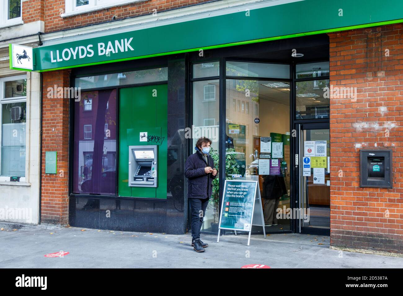 Un homme portant un masque attend à l'extérieur d'une succursale de Lloyds Bank pour observer les règles de distanciation sociale, Grays Inn Road, King's Cross, Londres, Royaume-Uni Banque D'Images