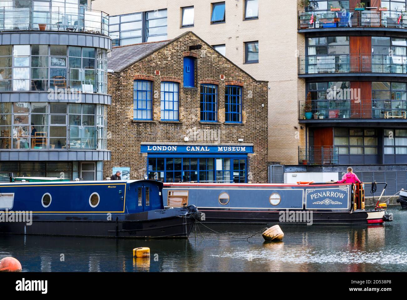 Une femme au pelage rose dirige un bateau à rames dans son amarrage à l'extérieur du London Canal Museum, Battlebridge Basin, King's Cross, Londres, Royaume-Uni Banque D'Images