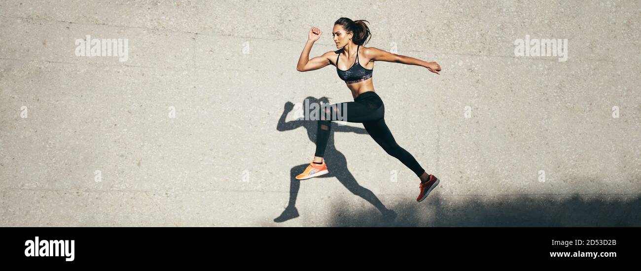 Jeune femme avec corps fit sauter et courir contre un arrière-plan gris. Modèle féminin dans l'exercice de sport en plein air. Banque D'Images
