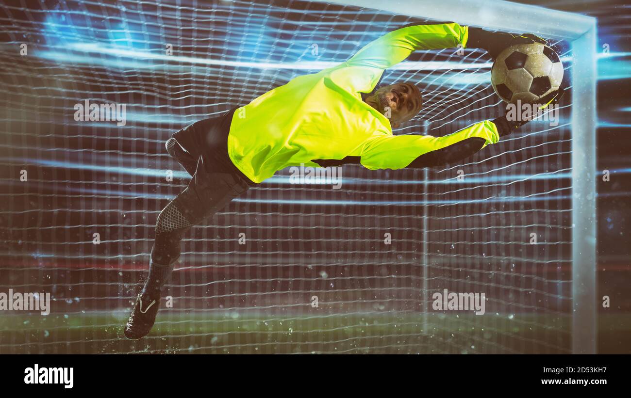 Gardien de but de football, en uniforme fluorescent, fait une économie et évite un but pendant un match de nuit Banque D'Images