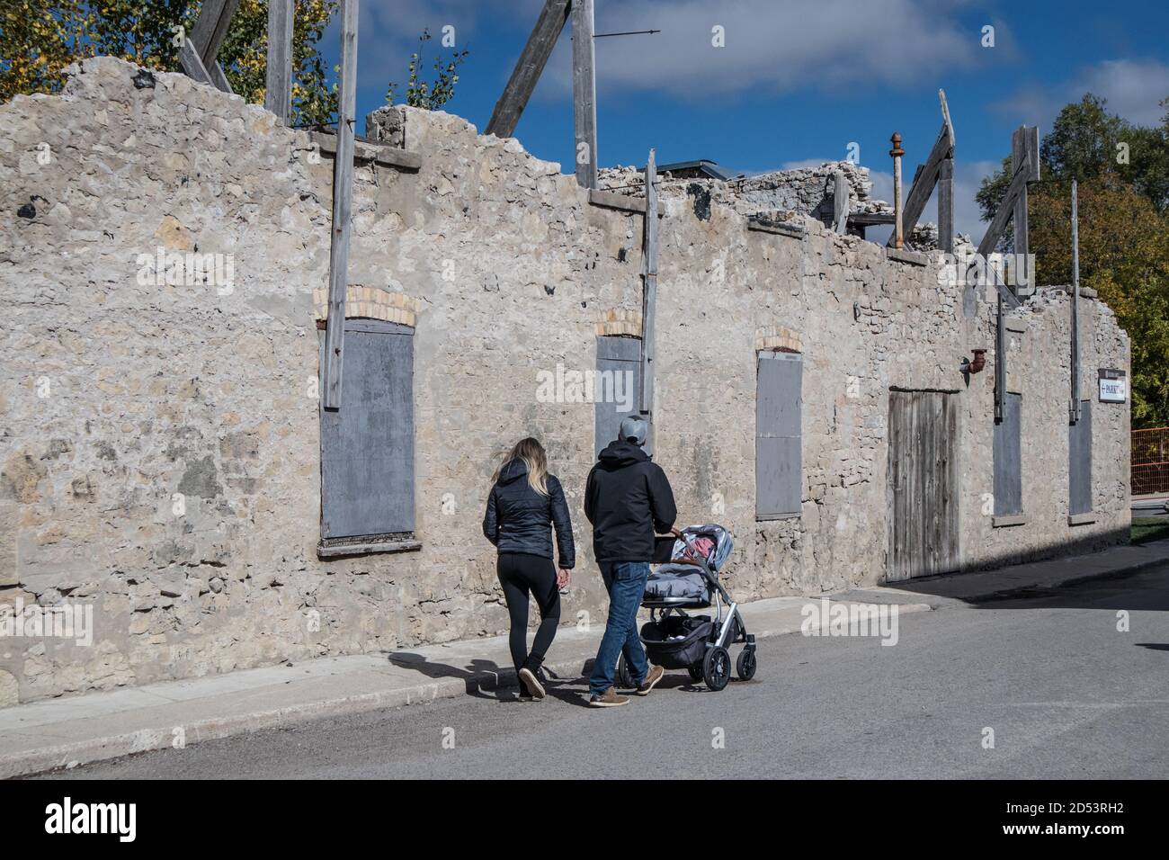 Un jeune couple avec leur enfant dans la poussette se promenant le long du mur de l'ancienne chapelle à Elora, en Ontario. Banque D'Images