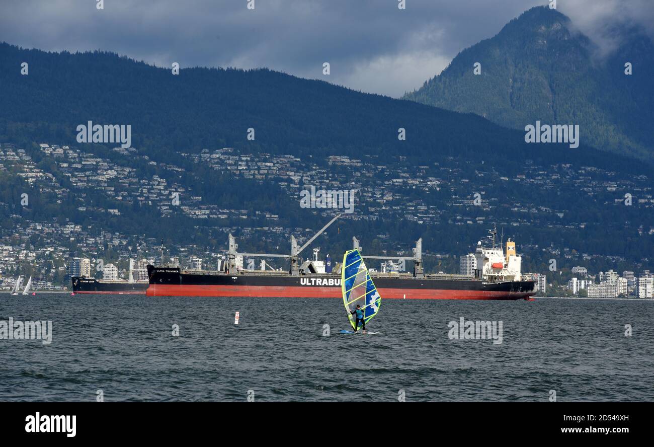 La planche à voile prend l'eau au large de la plage Jericho à Vancouver, Colombie-Britannique, Canada. À l'arrière-plan se trouvent les cargos et West Vancouver. Banque D'Images