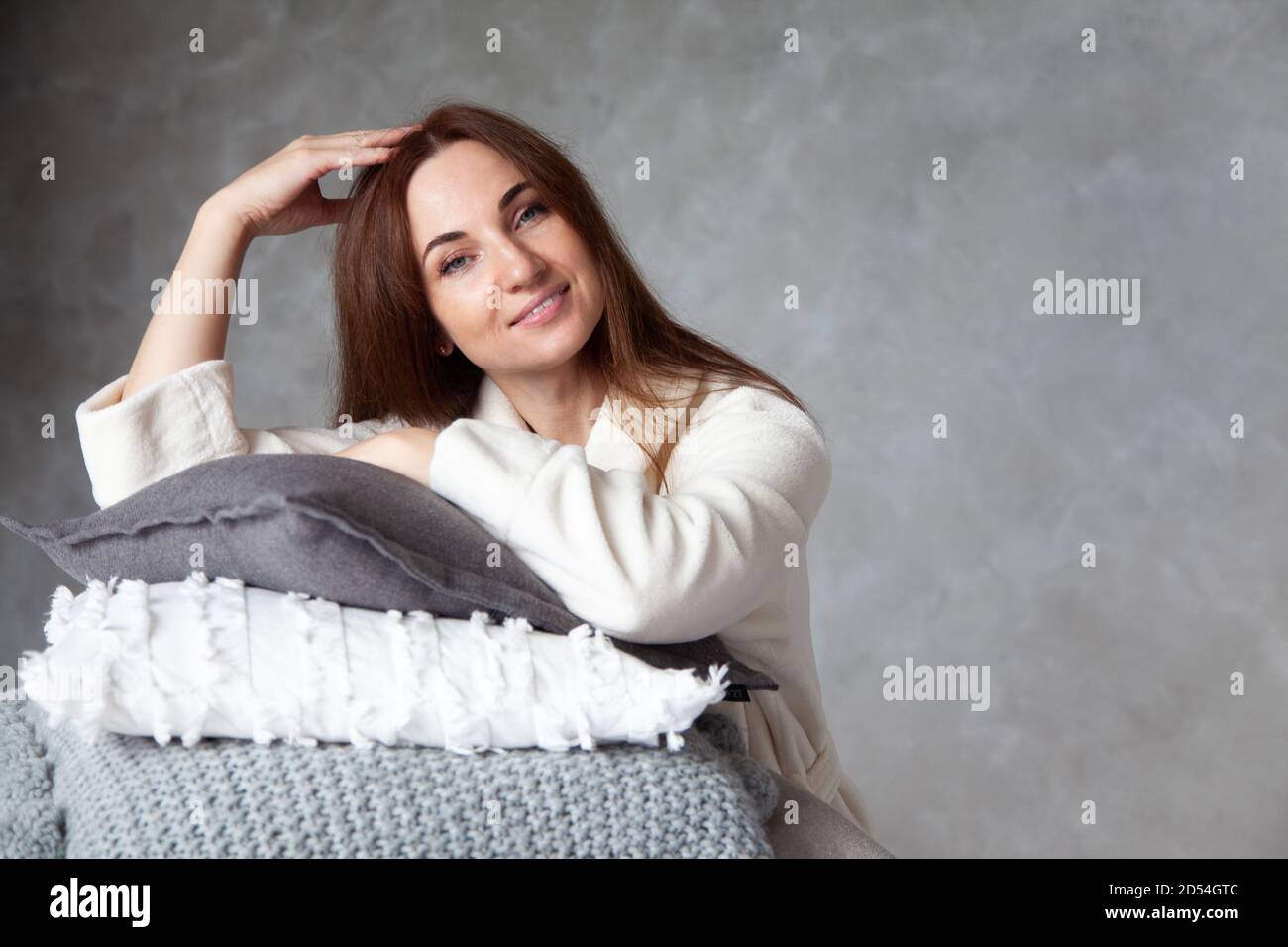 Jeune femme avec un beau sourire dans un peignoir beige chaud est s'appuyer sur une pile de draps pliés Banque D'Images