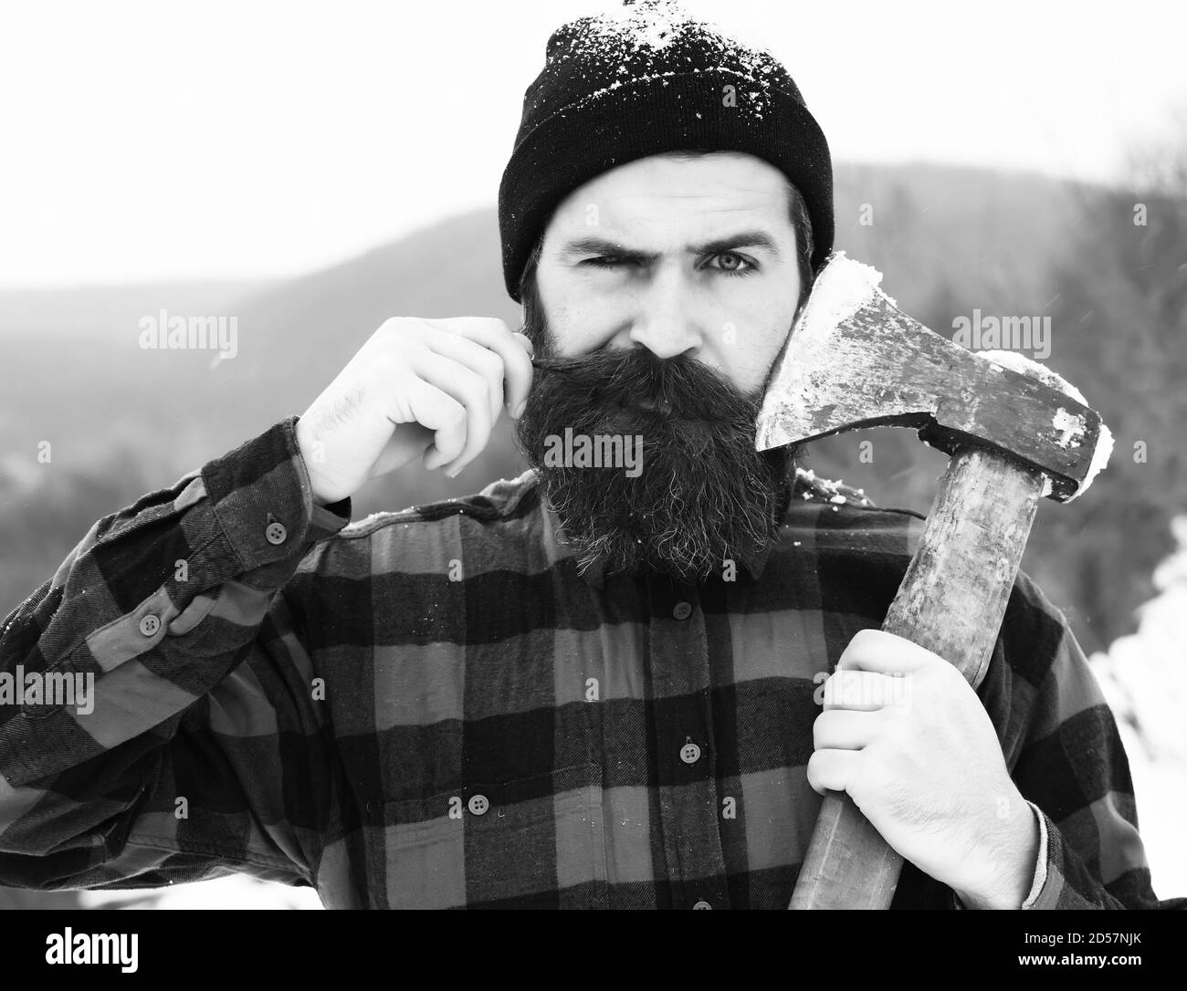 Un homme mouillé ou un bûcheron brutal, un hipster barbu, avec une barbe et une moustache en chemise à carreaux rouges, se rase avec une lame hache dans une forêt enneigée lors de la journée d'hiver en plein air sur fond naturel Banque D'Images
