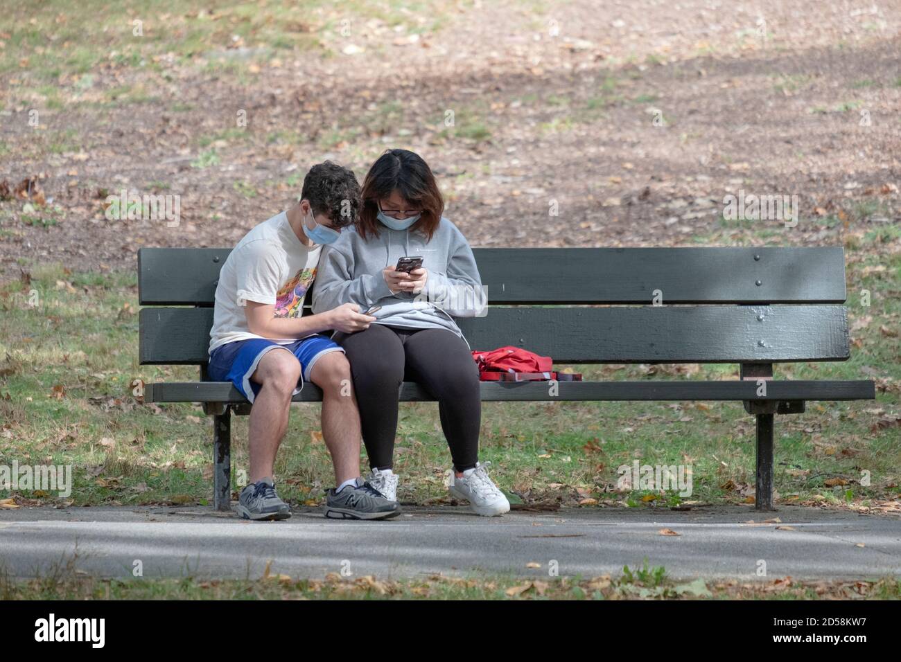 Un jeune couple s'assoit ensemble sur un banc de parc, chacun immergé avec son propre téléphone cellulaire. À Flushing, Queens, New York City.Wears, port Banque D'Images