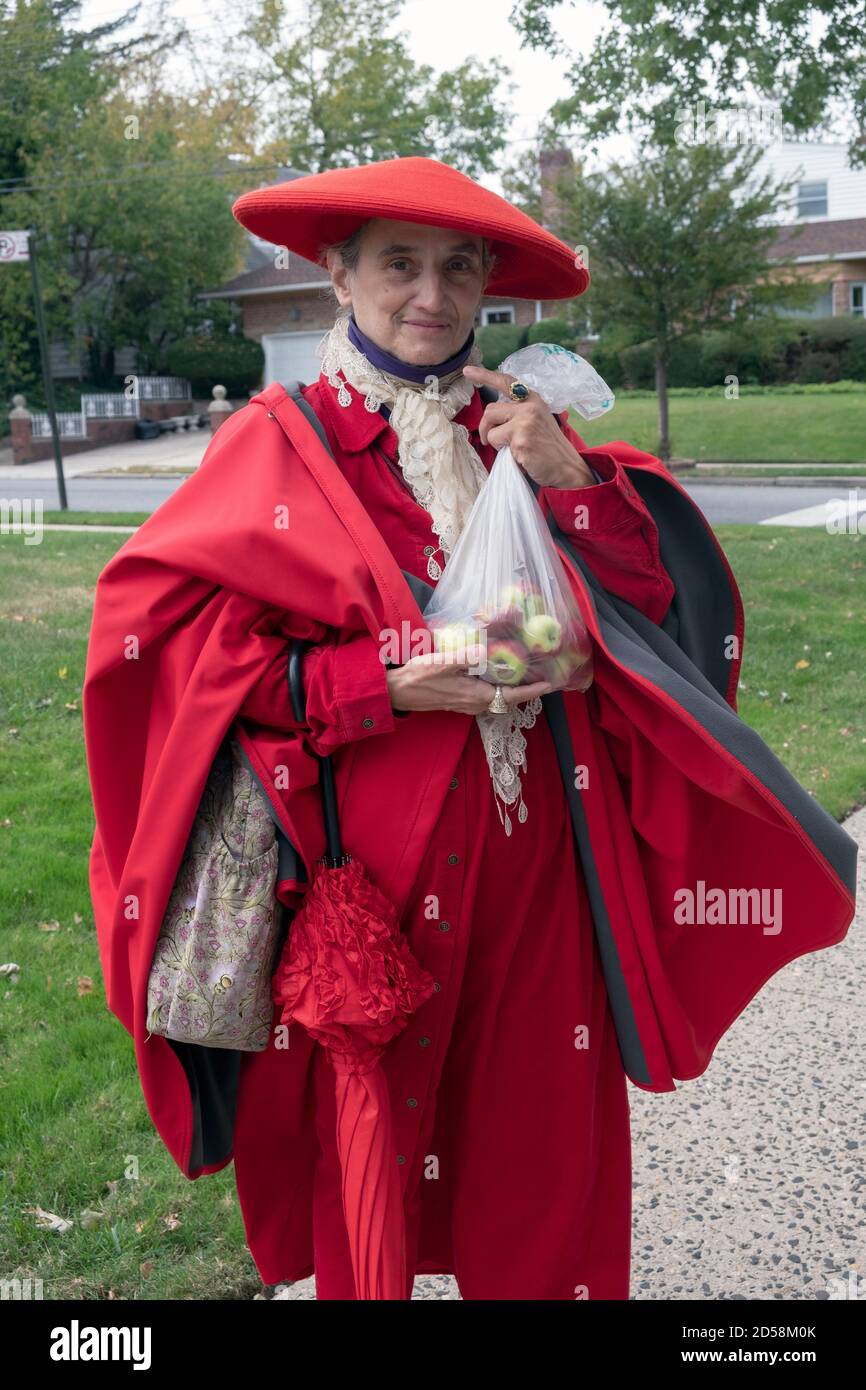 Une femme presque entièrement vêtue de rouge tenant un paquet de pommes fraîches. À Queens, New York. Banque D'Images