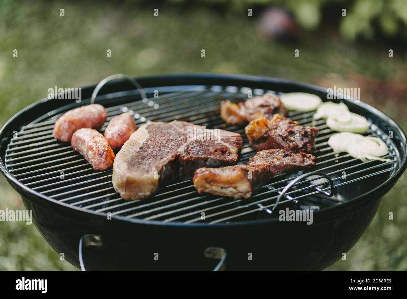 Steak, saucisses et oignons cuisant sur un barbecue Banque D'Images