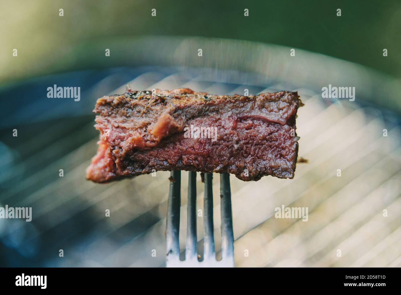 Morceau de steak sur une fourchette devant un barbecue Banque D'Images