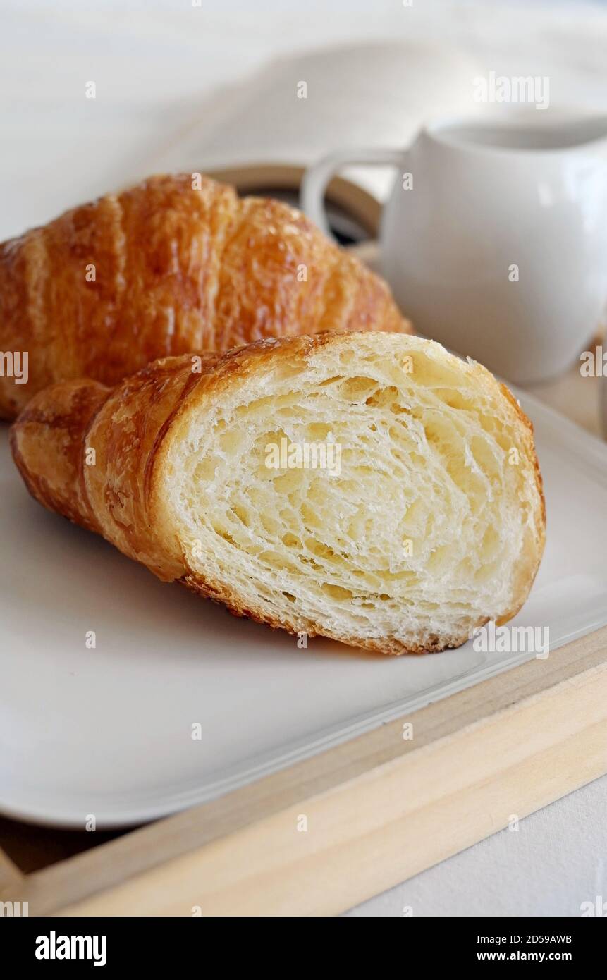 Gros plan d'un croissant en deux sur un plateau de petit déjeuner avec un livre et une verseuse Banque D'Images Gros plan d'un croissant en deux sur un plateau de petit déjeuner avec un livre et une verseuse Banque D'Images