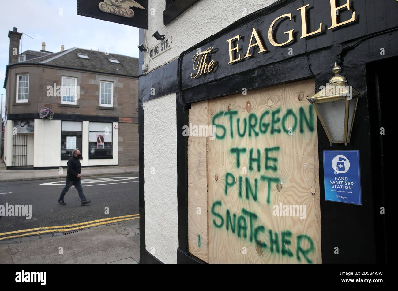 Un membre du public passe devant l'Eagle Coaching Inn à Broughty Ferry, où des graffitis ont été écrits à l'embarquement au-dessus des fenêtres après l'entrée en vigueur d'une série de nouvelles restrictions visant à lutter contre l'augmentation des cas de coronavirus en Écosse. Banque D'Images