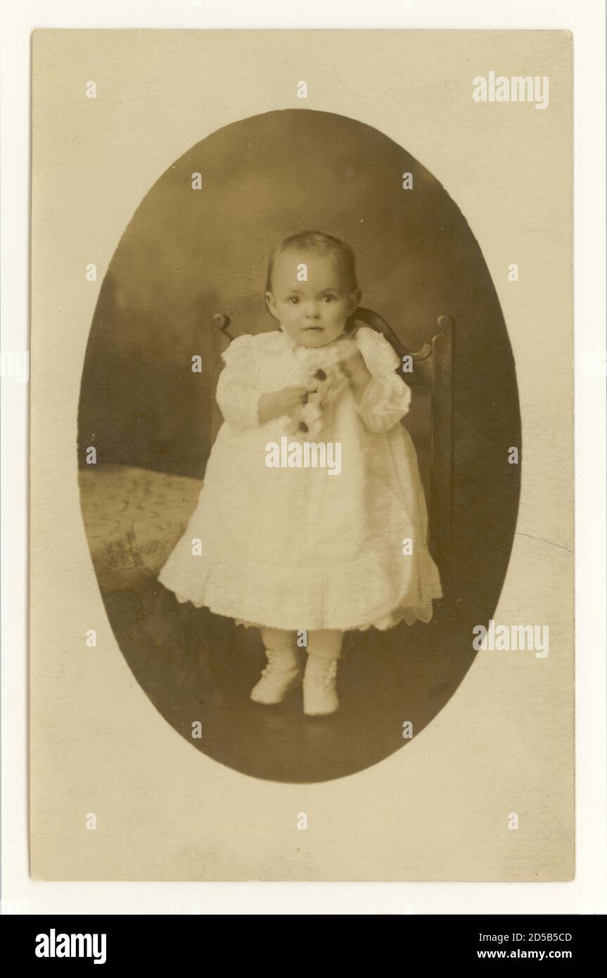 Début 1900 carte postale de bébé tout-petit, un an, tenant des fleurs artificielles prop R.-U. vers 1905 1906 Banque D'Images