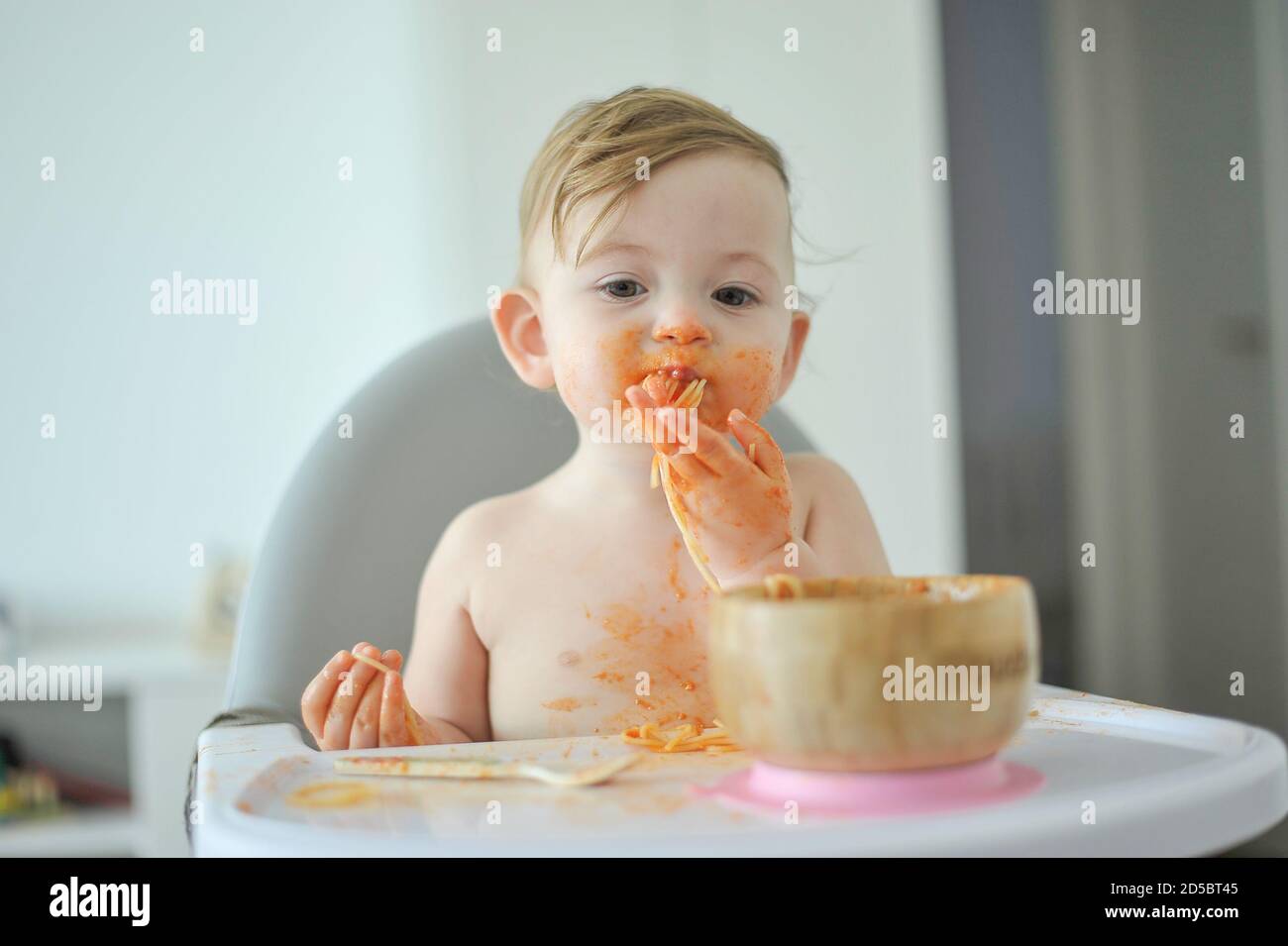 Bébé mangeant des pâtes assis sur une chaise haute Banque D'Images