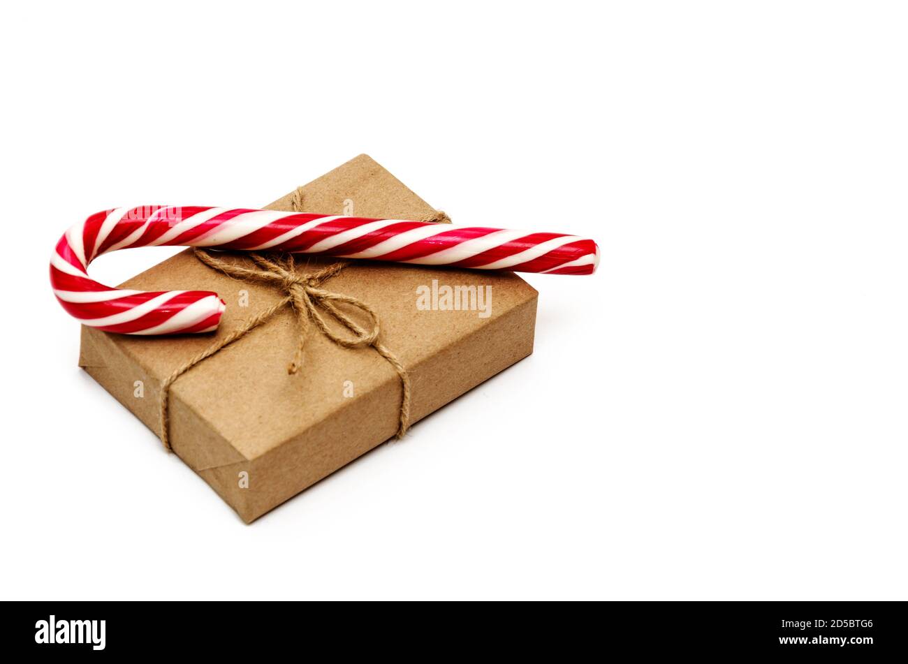 Boîte cadeau de Noël emballée dans du papier kraft attaché avec de la ficelle et de la canne à sucre sur fond blanc. Concept de Noël, d'hiver et de nouvel an Banque D'Images