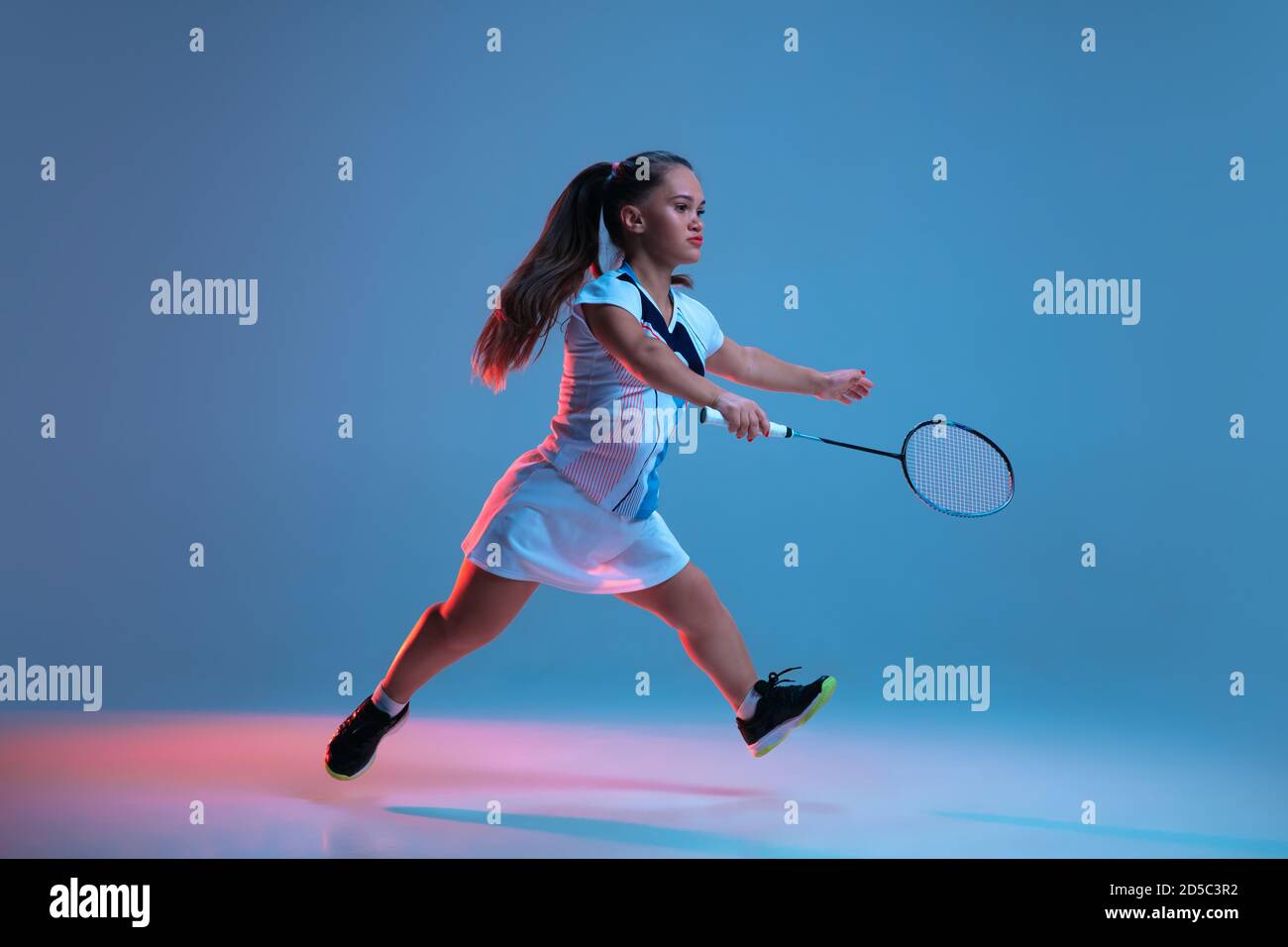 Haut. Belle femme naine pratiquant au badminton isolée sur fond bleu à la lumière du néon. Le style de vie des personnes inclusives, la diversité et l'équility. Sport, activité et mouvement. CopySpace. Banque D'Images