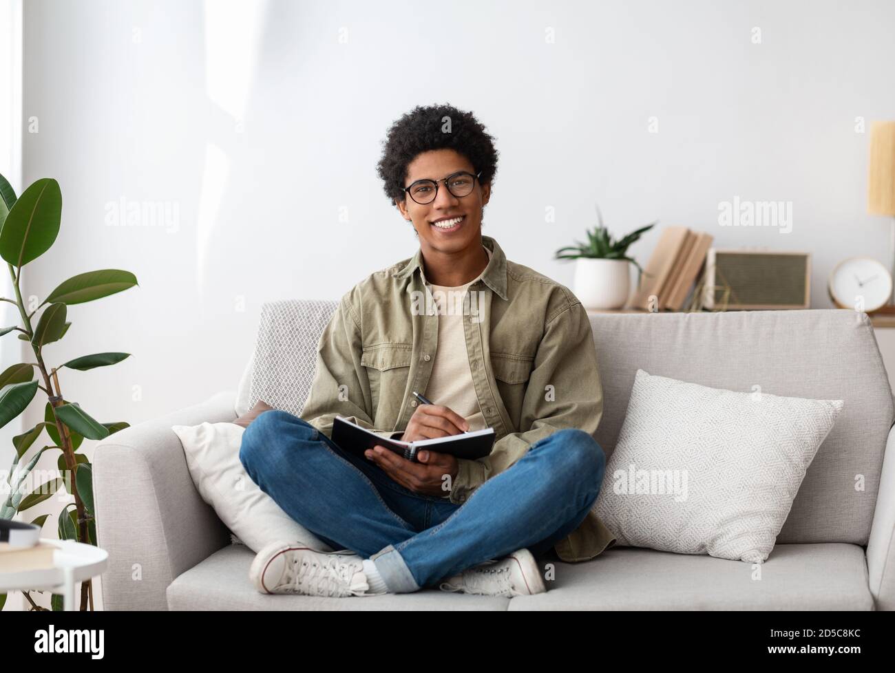 Joyeux adolescent étudiant avec un ordinateur portable assis sur le canapé et regarder l'appareil photo à l'intérieur Banque D'Images