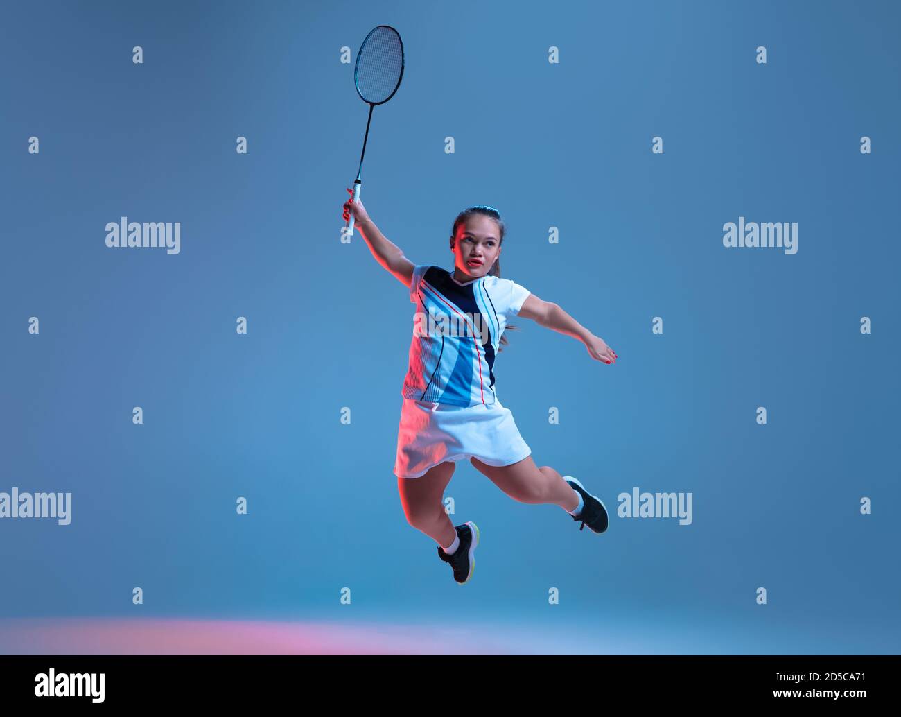 Fort. Belle femme naine pratiquant au badminton isolée sur fond bleu à la  lumière du néon. Le style de vie des personnes inclusives, la diversité et  l'équility. Sport, activité et mouvement. CopySpace