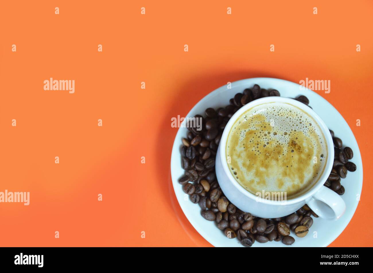 une tasse de café cappuccino avec de la crème chaude dans une tasse blanche sur fond orange avec des grains de café et une cuillère à café. vue du dessus. Banque D'Images