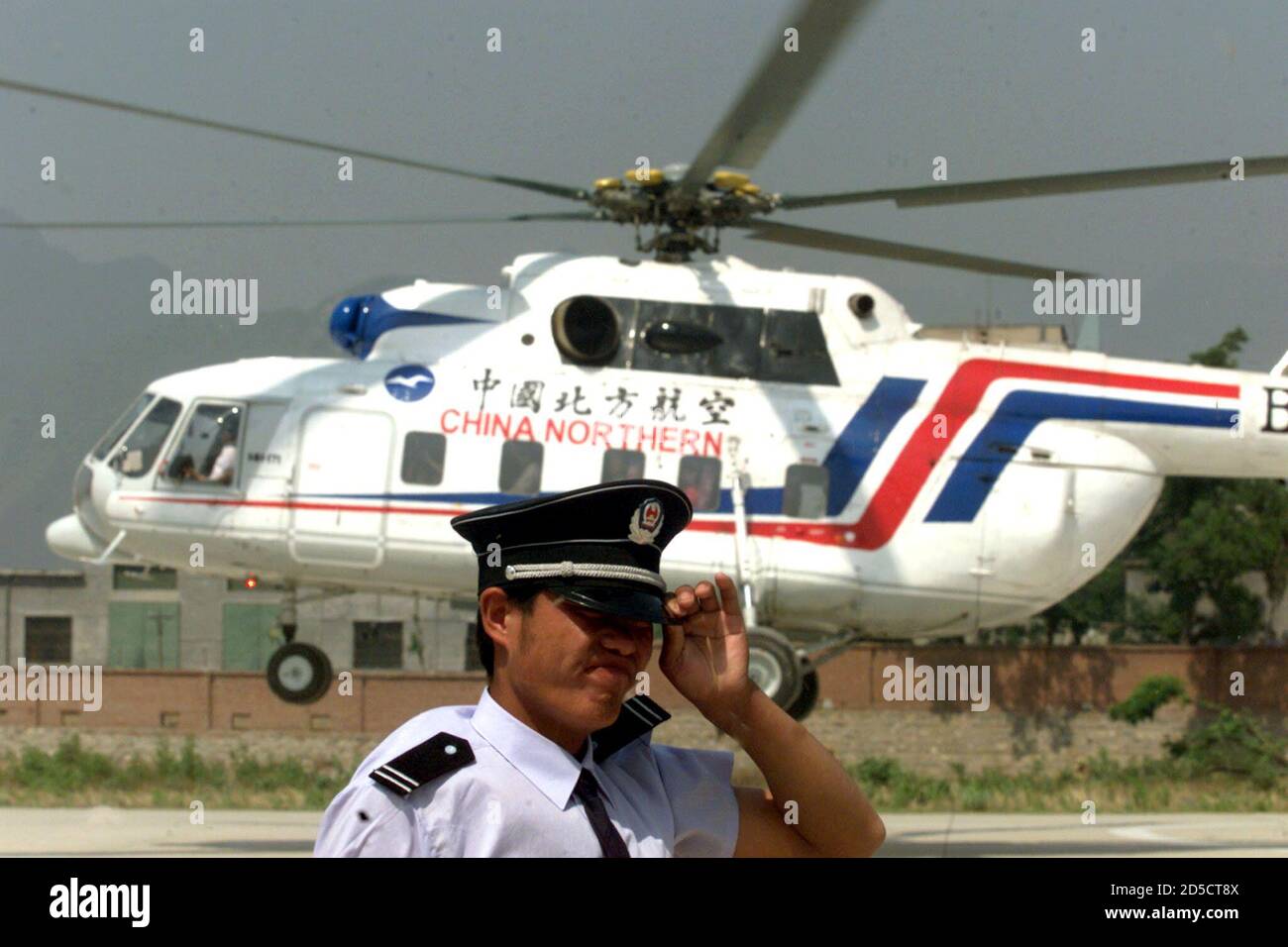 Un garde-fou chinois tient son chapeau alors qu'un hélicoptère transportant  des touristes se met en route pour une mission de tourisme à la Grande  Muraille, au nord de Pékin, en mai 20.