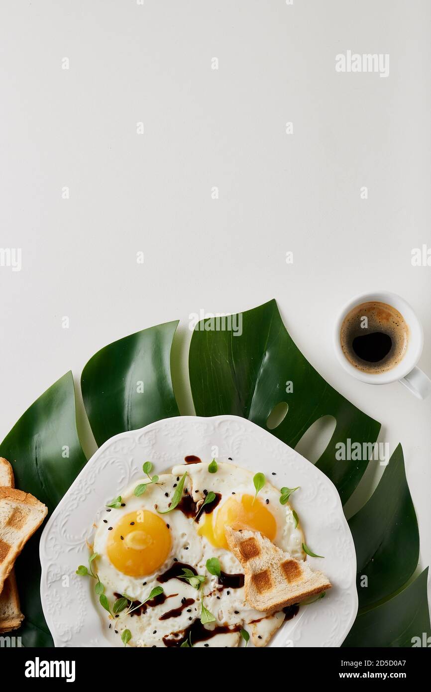 Petit déjeuner avec œufs frits, pain grillé et café blanc coupe et plante la feuille sur la table blanche Banque D'Images