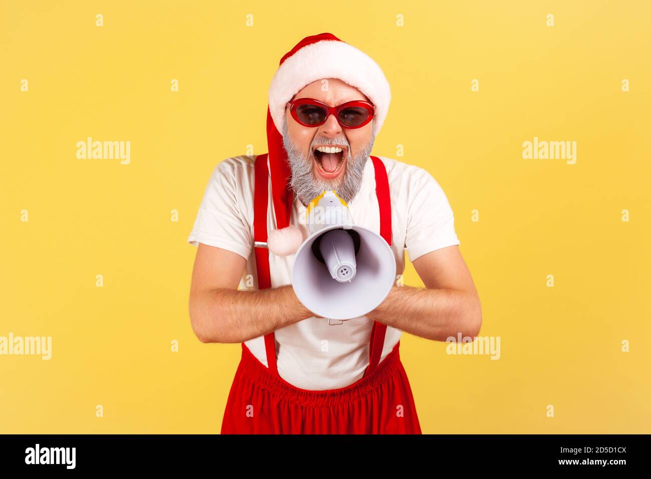 Un homme à barbe grise et affectif en costume du père noël criant au haut-parleur, félicite pour ses vacances, fête de fantaisie. Prise de vue en studio en intérieur isola Banque D'Images