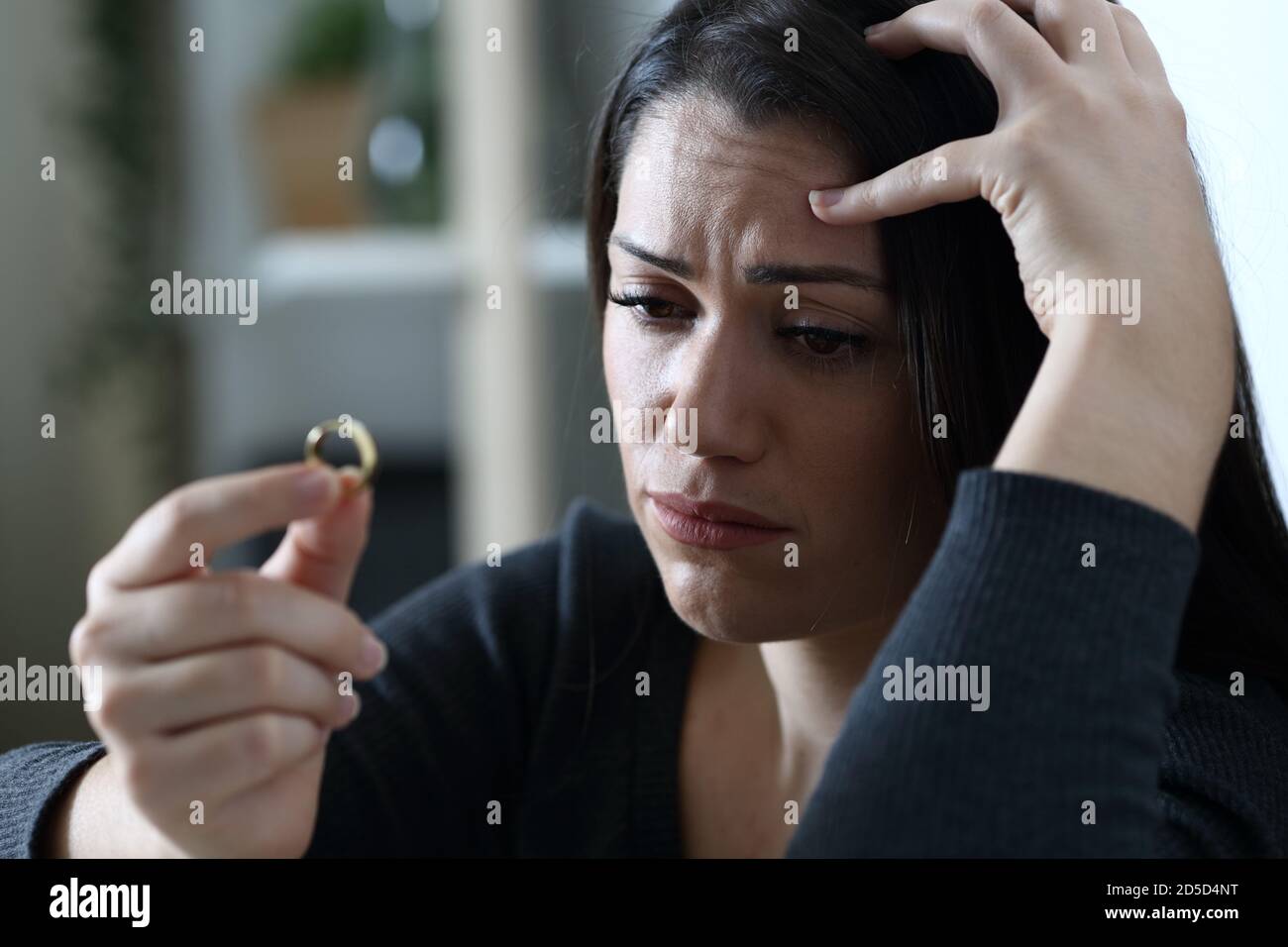 Triste femme douteuse regarde l'anneau de mariage de la pensée dans le divorce seul à la maison dans la nuit Banque D'Images