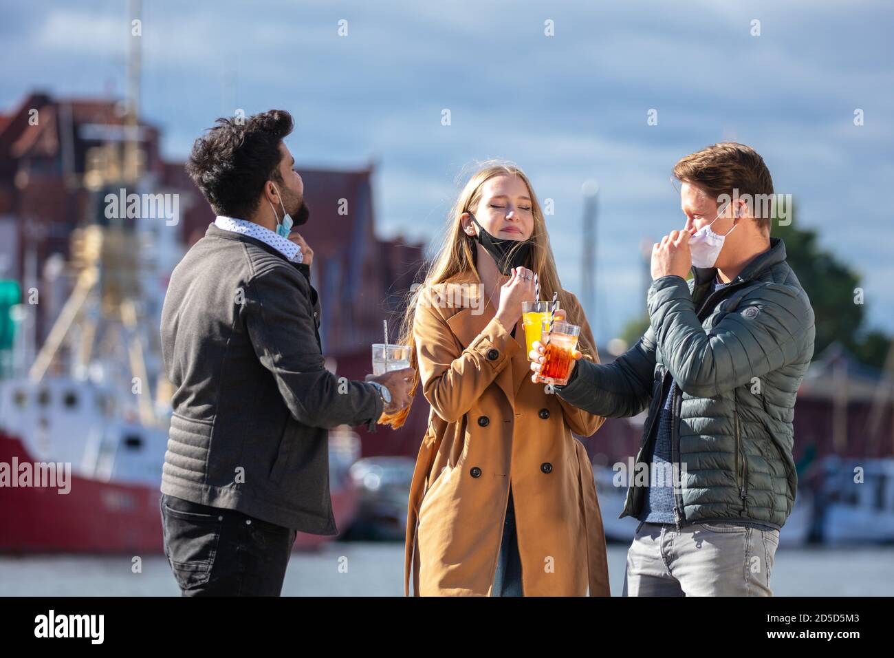 Zwei Männer und eine Frau in Corona-Zeit, mit alltäglichen Masken, in der kalten Jahreszeit in der Stadt unterwegs. Getränke im Freien. Banque D'Images