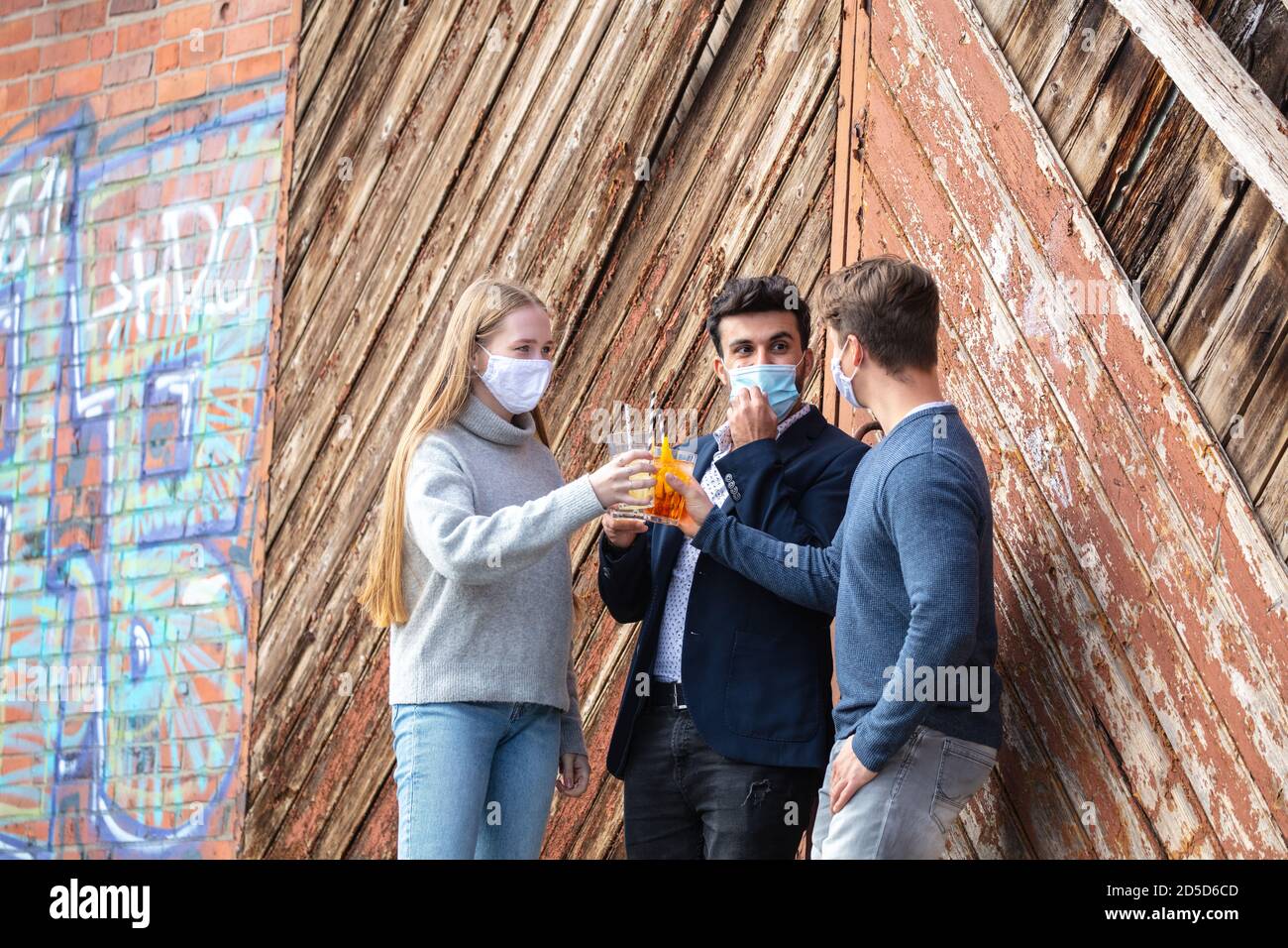 Gruppe junger Menschen zur Cornazeit mit Alltagsmaske, Freizeit in der Stadt mit Maske. Stöhner mit Getränk im freien. Banque D'Images