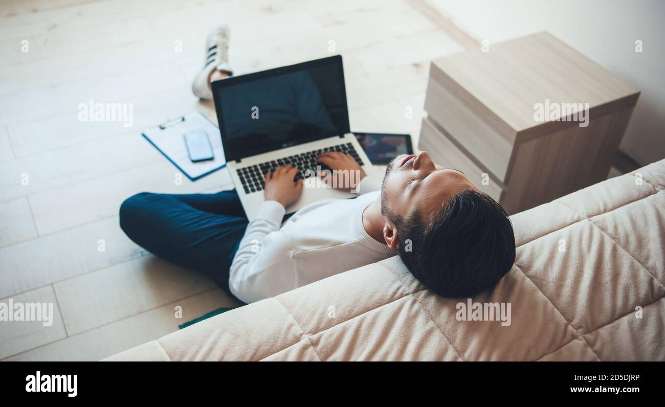 Un jeune homme d'affaires du caucase se sentait fatigué après avoir travaillé sur l'ordinateur portable de la maison assis sur le sol près du lit tombant endormi Banque D'Images