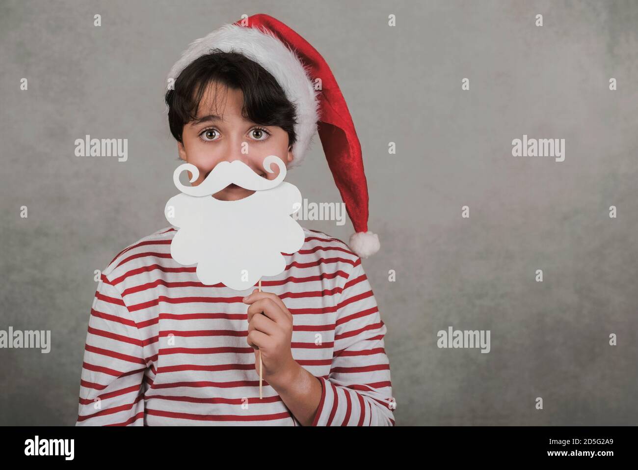 Joyeux Noël, jeune fille souriante portant le chapeau de Noël du Père Noël avec faux barbe sur bâton sur fond gris Banque D'Images