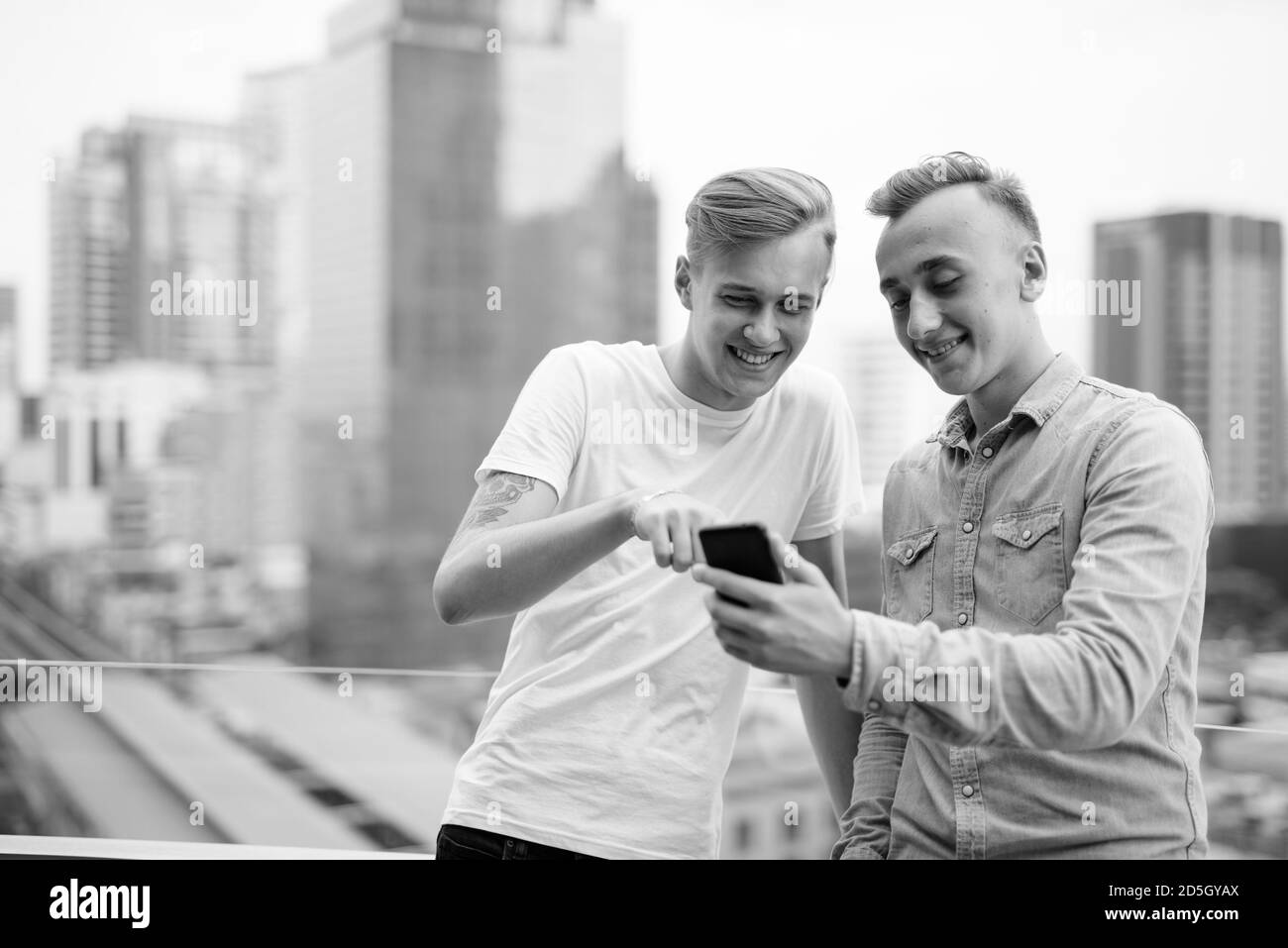 Deux jeunes hommes beaux avec des cheveux blonds ensemble contre la vue de la ville Banque D'Images