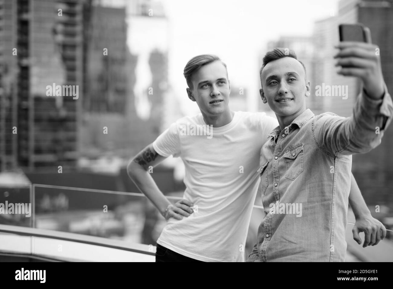 Deux jeunes hommes beaux avec des cheveux blonds ensemble contre la vue de la ville Banque D'Images