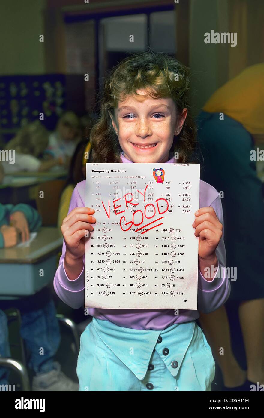 Une étudiante souriante de 3e année montre et affiche un le papier scolaire dit très bien Banque D'Images Une étudiante souriante de 3e année montre et affiche un le papier scolaire dit très bien Banque D'Images