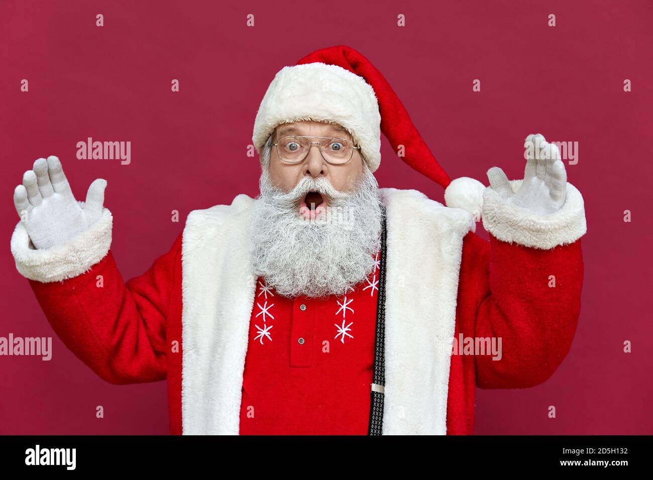 Le père Noël drôle et stupéfait portait un costume isolé sur fond rouge. Banque D'Images
