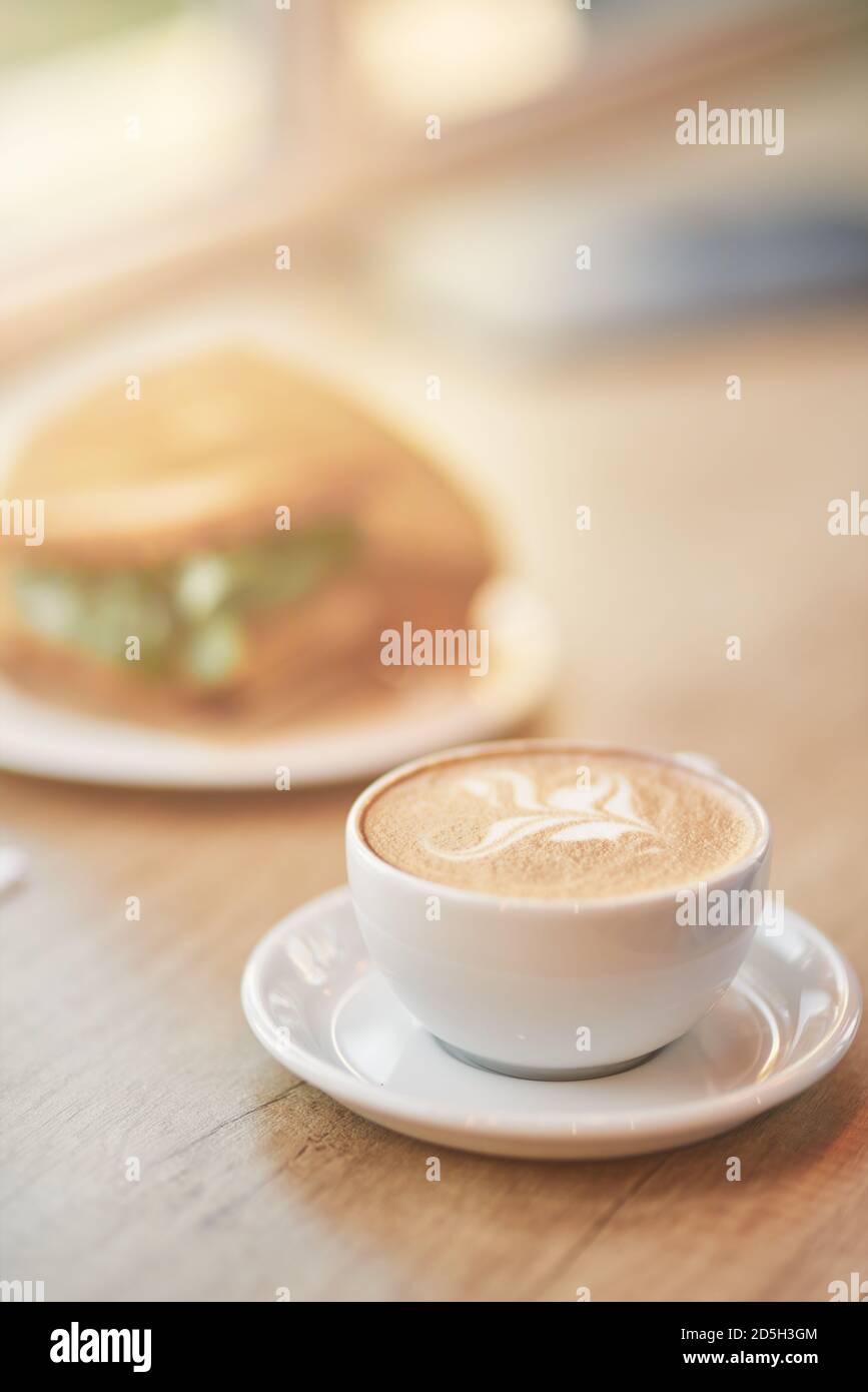 Gros plan vertical d'une tasse de café cappuccino et sandwich sur une table en bois dans le café, mise au point sélective Banque D'Images