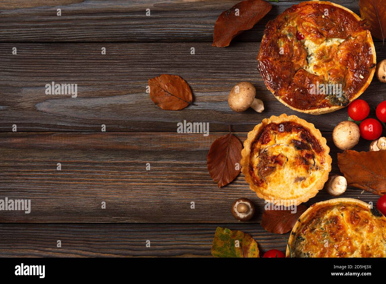 Quiche de pâtisserie maison lorraine aux épinards, aux champignons, aux tomates et au fromage sur une table en bois avec feuilles d'automne. Vue sur le dessus avec espace copie Banque D'Images