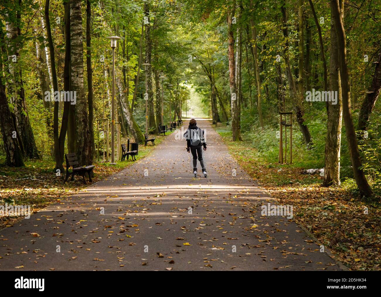 une jeune fille se déplace sur des patins à roulettes le long du chemin déserté de le parc d'automne Banque D'Images