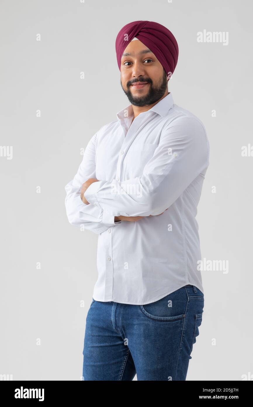 SIKH HOMME DEBOUT AVEC LES BRAS CROISÉS SOURIANT REGARDANT DANS LE APPAREIL PHOTO Banque D'Images